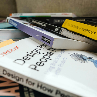 A stack of design and branding books, including titles like “Design for People” and “The Design of Everyday Things,” placed on a table.