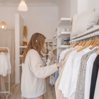 Woman browsing clothing in a bright, minimalist boutique with white walls and neatly arranged racks.