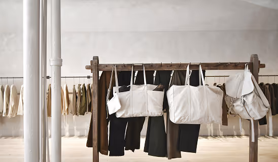 Minimalist store interior with wooden rack holding tote bags and clothing in neutral tones.