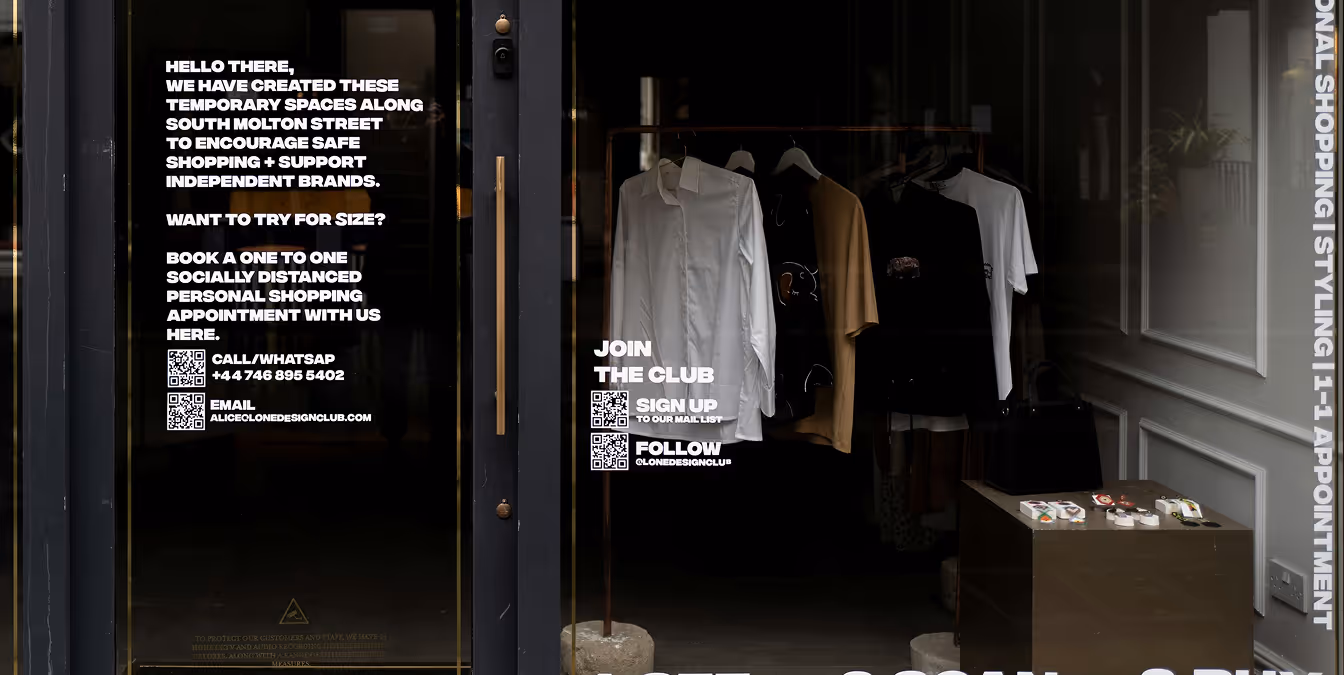 Storefront window with white text promoting independent brands, showing shirts and accessories displayed inside.