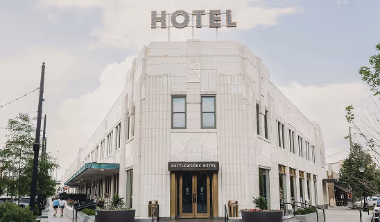 Exterior of an art-deco style hotel with large “HOTEL” sign on the roof and a main entrance reading “Bottleworks Hotel.”