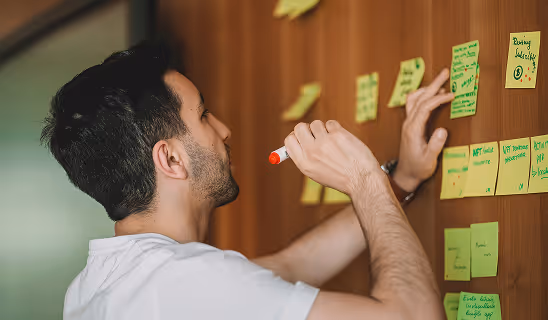 Man writing ideas on sticky notes attached to a wall, engaged in creative brainstorming.