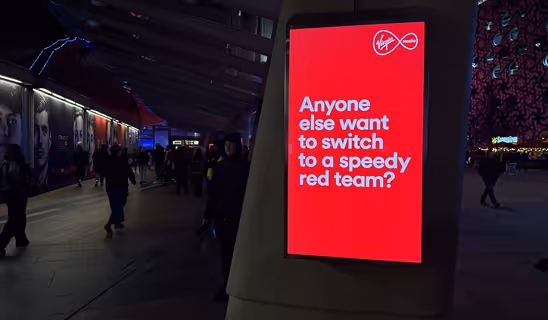 Outdoor digital billboard with Virgin Media’s red ad reading “Anyone else want to switch to a speedy red team?”