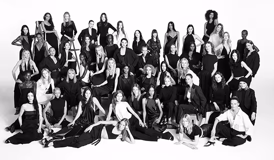 Black-and-white group portrait of a large number of models dressed in elegant black outfits, posed in rows.