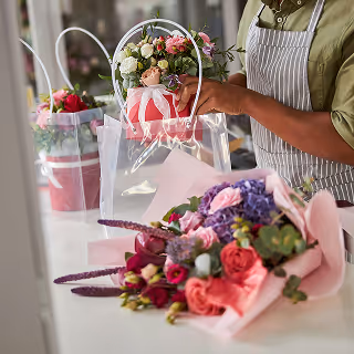 Florist arranging fresh flowers in a bouquet, with other colorful floral arrangements on the counter.