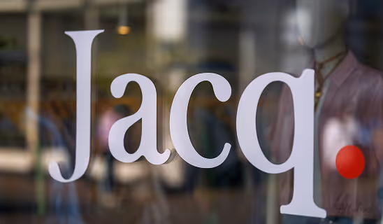 Close-up of a store window displaying the name “Jacq.” in white text with a red dot accent.