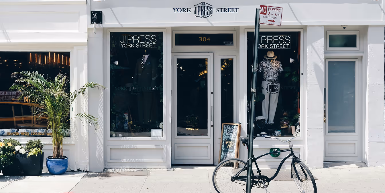 Exterior of a clothing store with “J. Press York Street” signage, large display windows, and a bicycle parked out front.