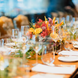 Long dining table set with wine glasses, plates, and a vibrant floral centerpiece in warm lighting.