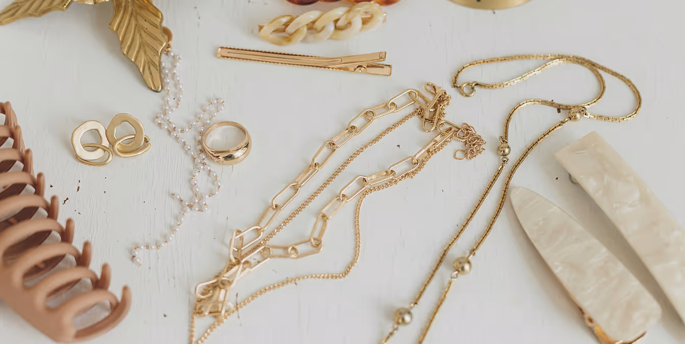 Flat lay of gold necklaces, rings, pearl chains, and decorative hair clips arranged on a white surface.