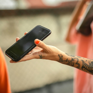 Close-up of a hand with tattoos and painted nails holding a black smartphone.