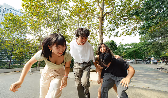 Four young adults playfully running together on a sunny day in a park.