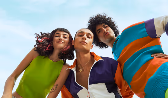 Young adults in colorful clothing posing confidently against a bright blue sky.