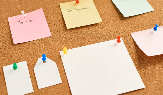 A corkboard with colorful sticky notes labeled “To Do” and “In Progress,” along with blank notes, pinned in place.