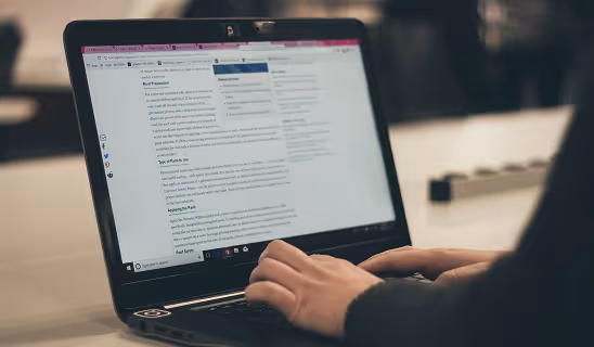 A close-up of hands typing on a laptop displaying a blog post editor interface.