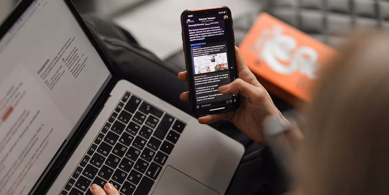 A person holding a smartphone displaying a messaging app while working on a laptop.