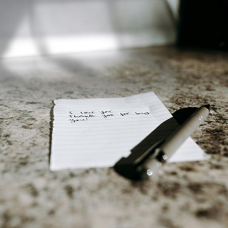 A piece of lined paper with a handwritten note reading “I love you. Thank you for being you” next to a pen.