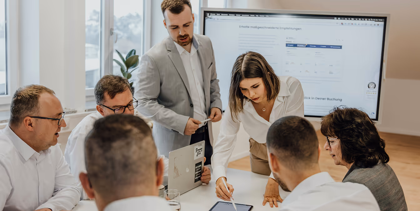A businesswoman pointing at a tablet while discussing a project with a group of colleagues around a conference table in a modern office.