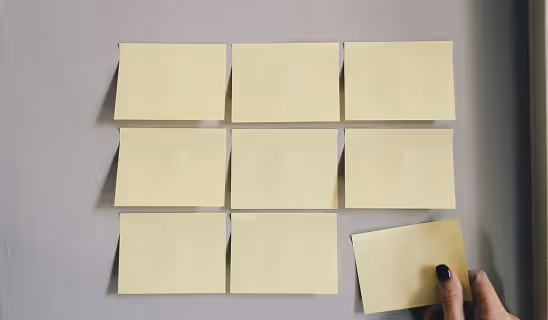 Hand placing a yellow sticky note among neatly arranged notes in a grid pattern on a wall.