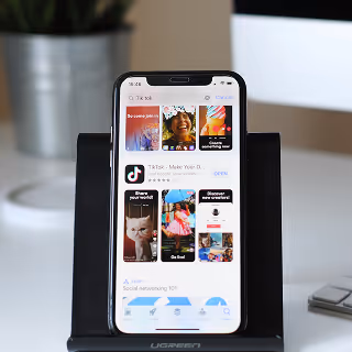 iPhone on a desk stand showing the TikTok app store page with featured videos and download option.