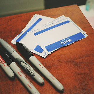 Close-up of blank "Hello" name tags with Sharpie markers on a wooden surface.
