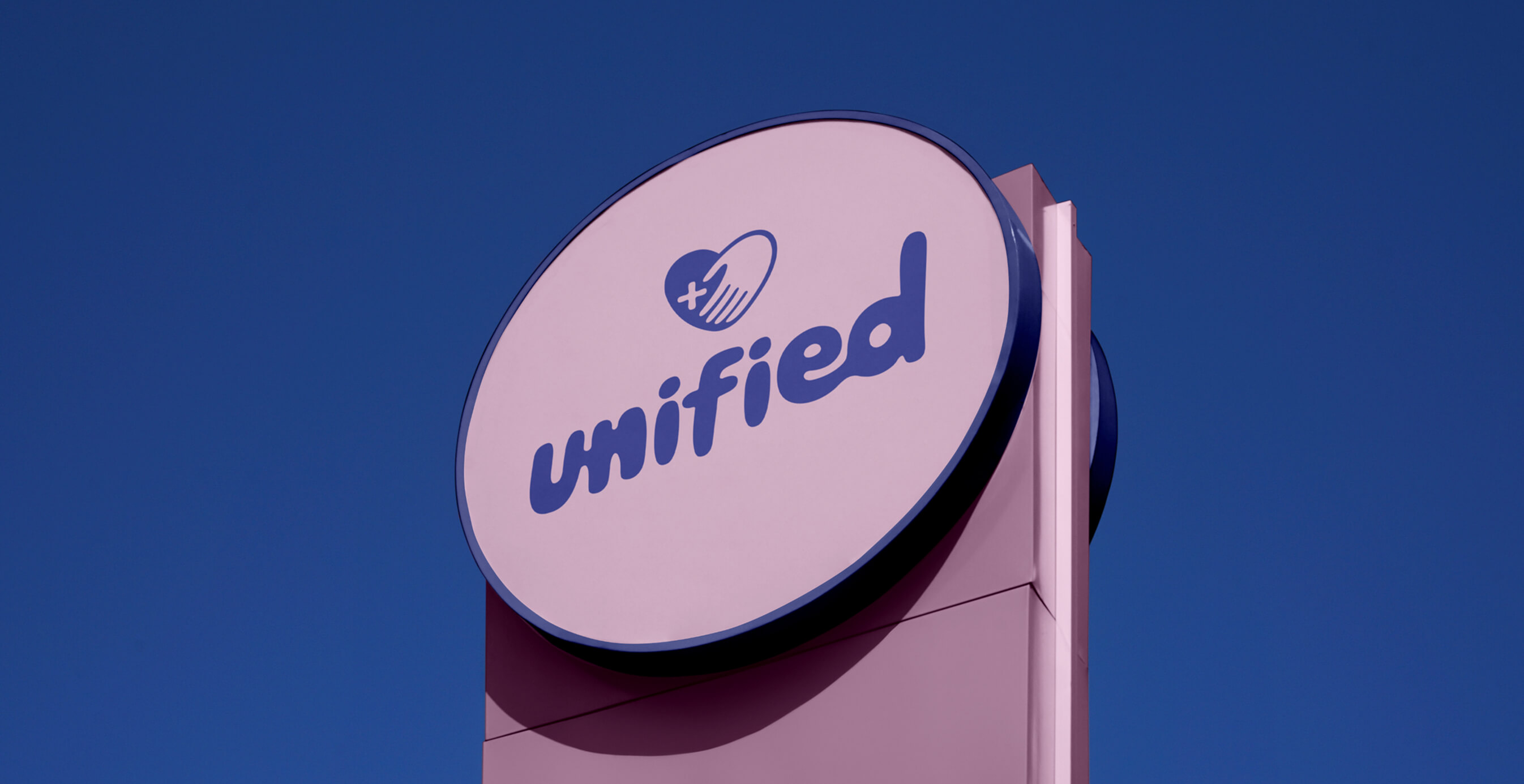 Round outdoor sign with Unified logo in purple and pink against a clear blue sky.