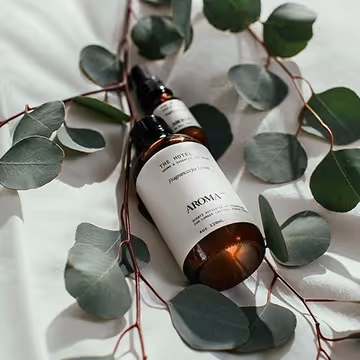 A flat-lay arrangement of Aroma-branded amber bottles with white labels placed among eucalyptus leaves, styled for a natural wellness aesthetic.