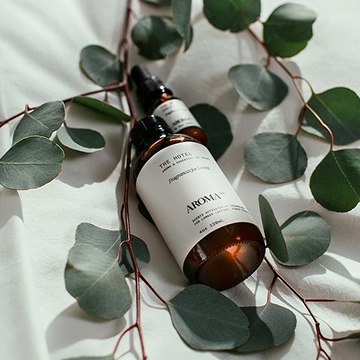 A flat-lay arrangement of Aroma-branded amber bottles with white labels placed among eucalyptus leaves, styled for a natural wellness aesthetic.