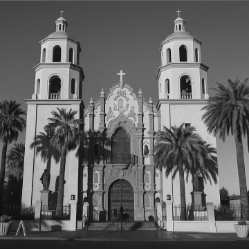 A black-and-white photo of St. Augustine Cathedral in Tucson, Arizona, with twin towers, palm trees, and ornate Spanish Colonial architecture.