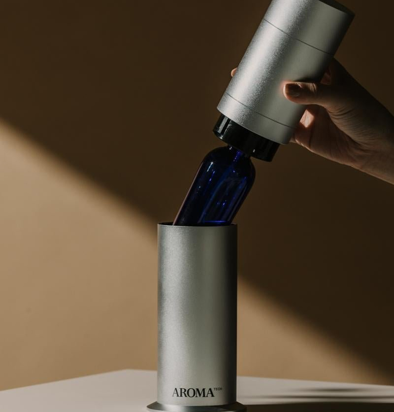 Hand inserting a blue essential oil bottle into a silver Aromatech diffuser.