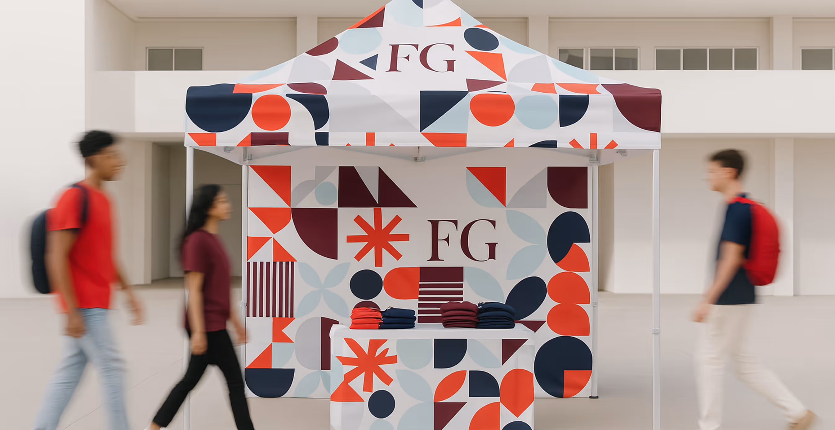 Fearless Grad promotional booth with geometric red, navy, and light blue patterns and “FG” logo, set up at a student event with people walking by.