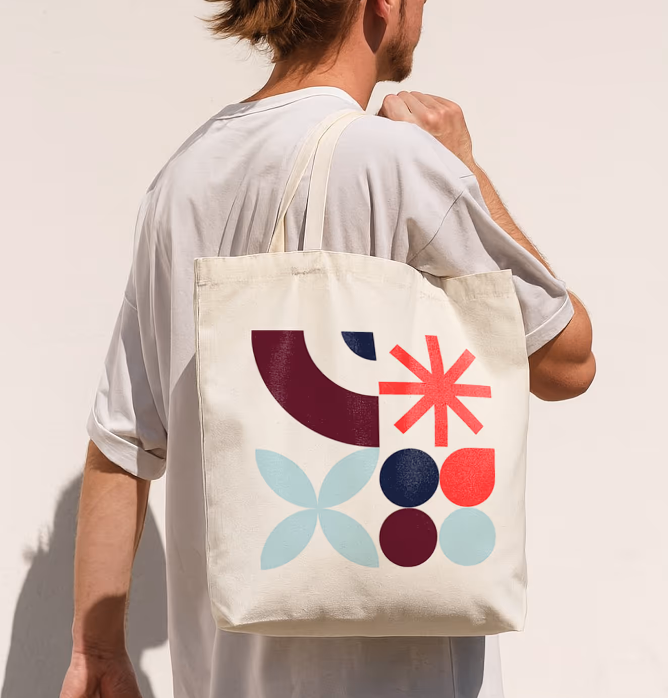 Man carrying a cream tote bag printed with Fearless Grad’s bold geometric shapes in red, navy, and teal.