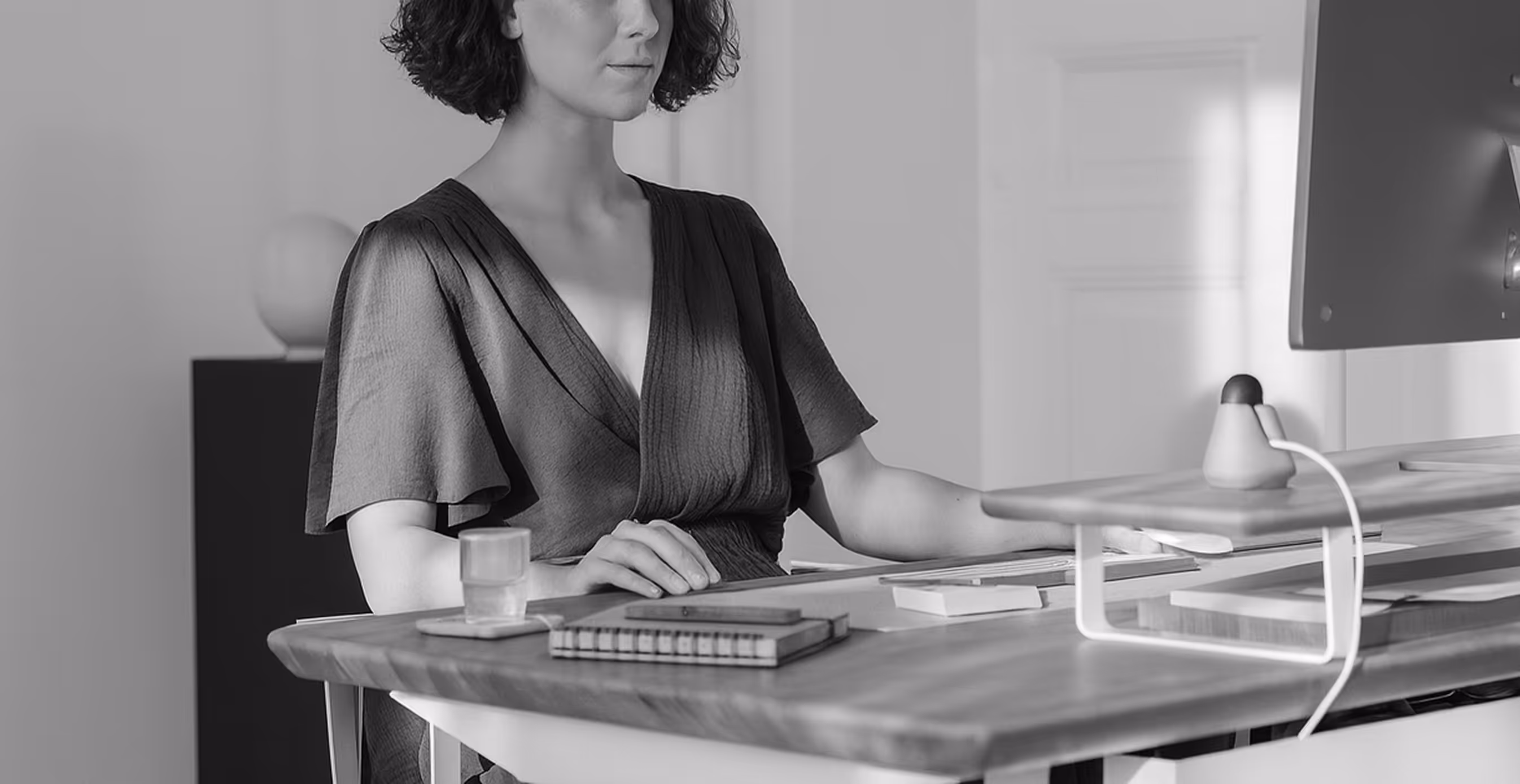 A woman works at a sleek HumanCentric desk setup with a monitor riser and organized workspace, showcasing focus and productivity.