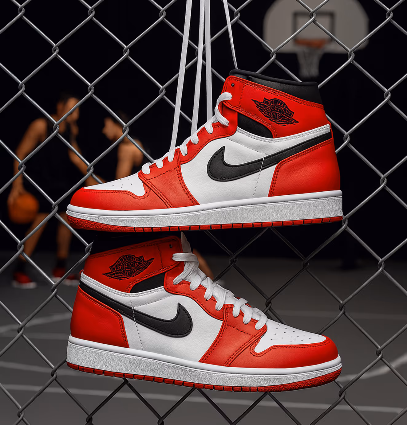 Pair of red, white, and black Nike Air Jordan sneakers hanging by their laces on a chain-link fence with basketball players blurred in the background.
