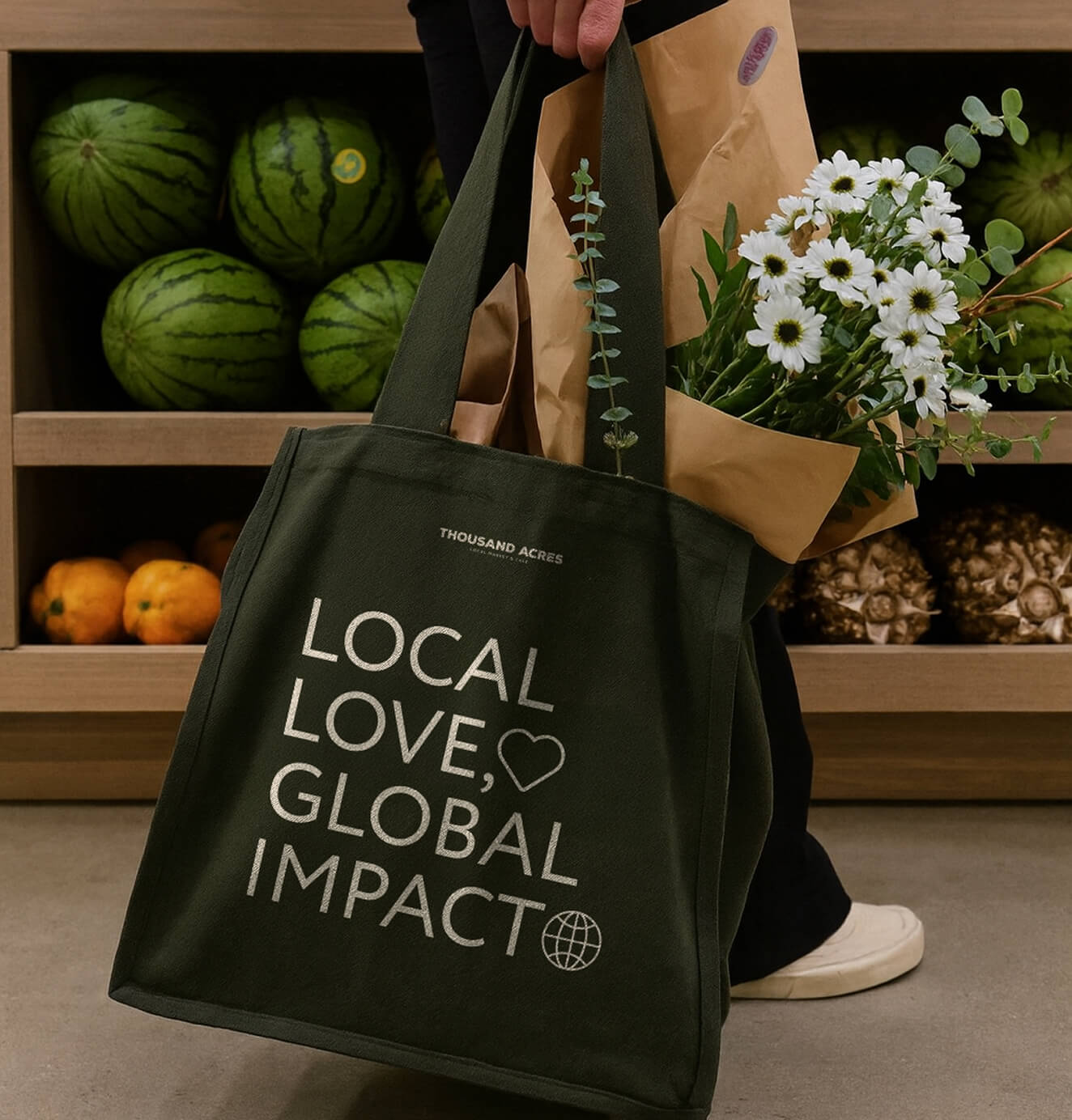 A dark green reusable tote bag with the words "Local Love, Global Impact" sits on the floor, filled with groceries and flowers.