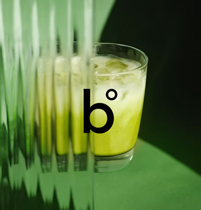 A glass of iced green matcha-style drink with the Bomi logo overlaid, reflected through a textured green surface.