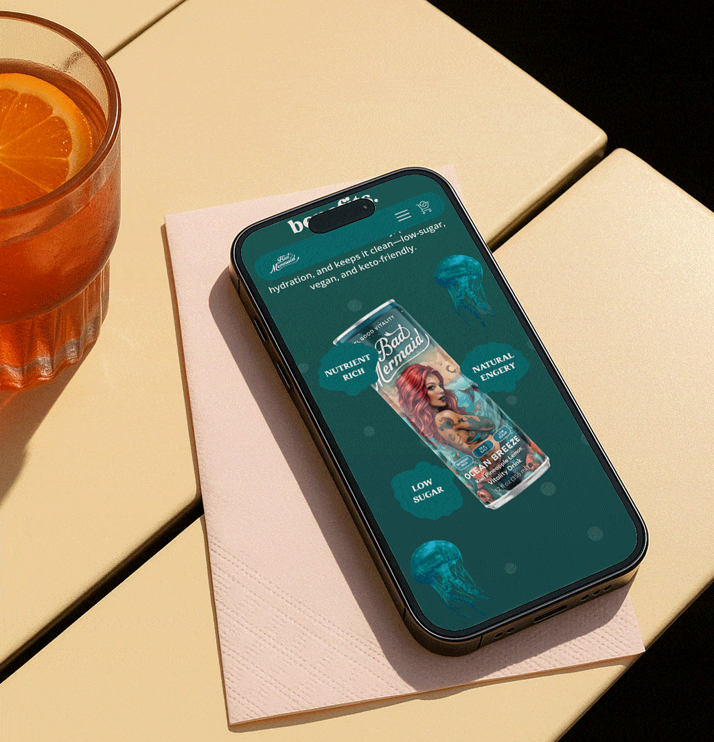 Animated GIF showing a smartphone on a café table next to a glass of orange drink. The phone screen displays a Bad Mermaid Ocean Breeze can with highlighted benefits such as nutrient-rich, low sugar, vegan, and natural energy.