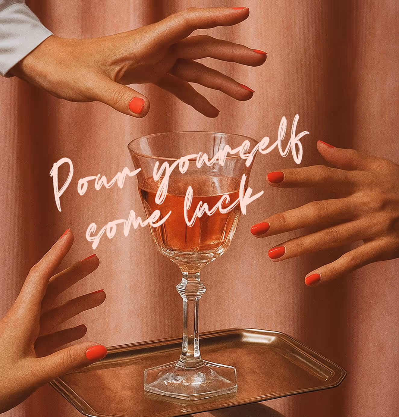A wine glass filled with rosé on a gold tray surrounded by hands with red-painted nails, overlaid with the text “Pour yourself some luck.”