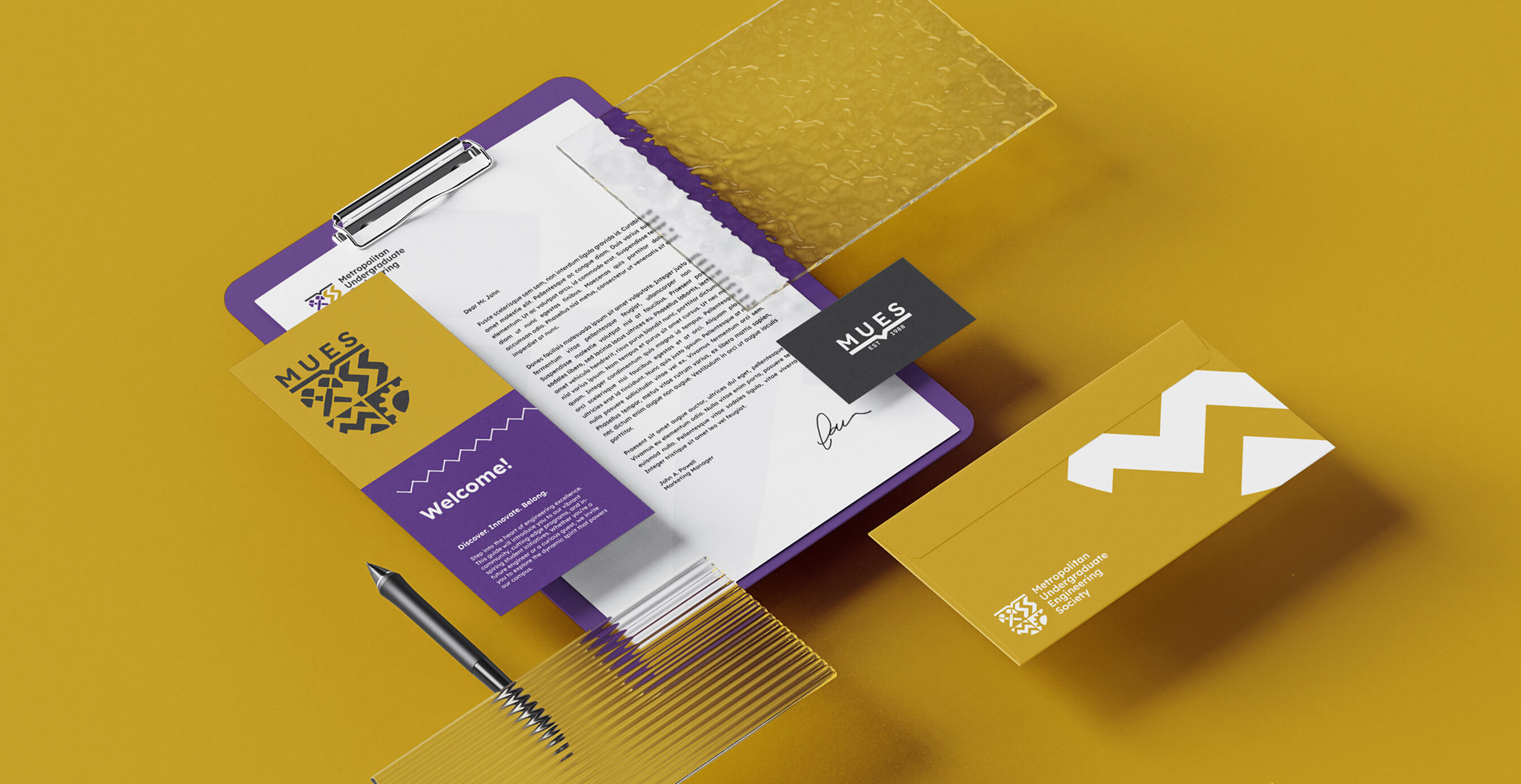 MUES branded stationery items on a gold background, including a clipboard with a welcome letter, purple and gold brochures, and a black business card.