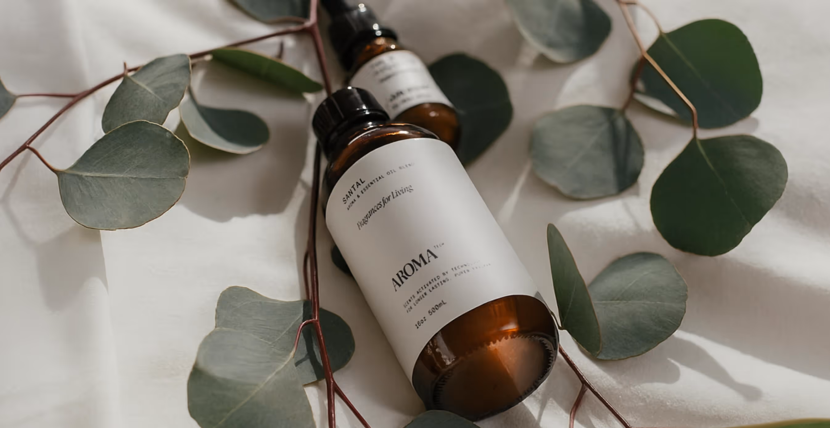 Aromatech essential oil bottles styled on white fabric surrounded by fresh eucalyptus leaves.
