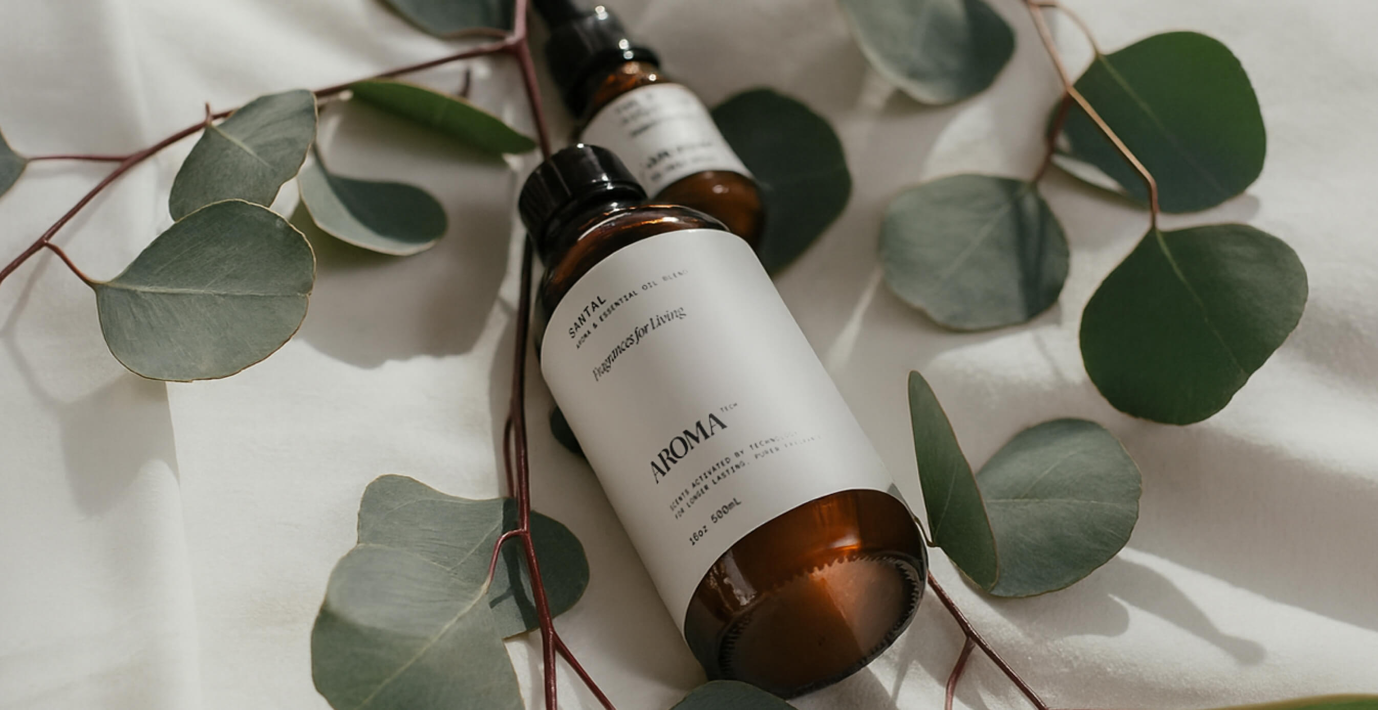 Aromatech essential oil bottles styled on white fabric surrounded by fresh eucalyptus leaves.