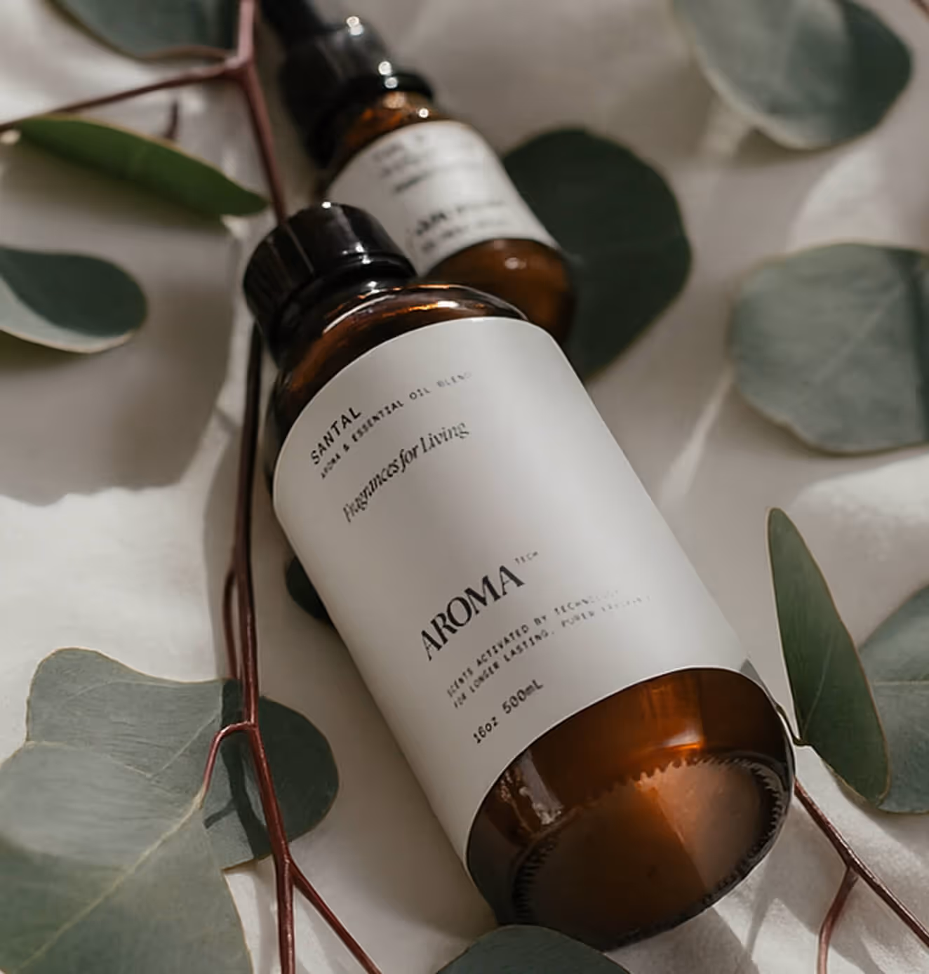 Aromatech essential oil bottles styled on white fabric surrounded by fresh eucalyptus leaves.