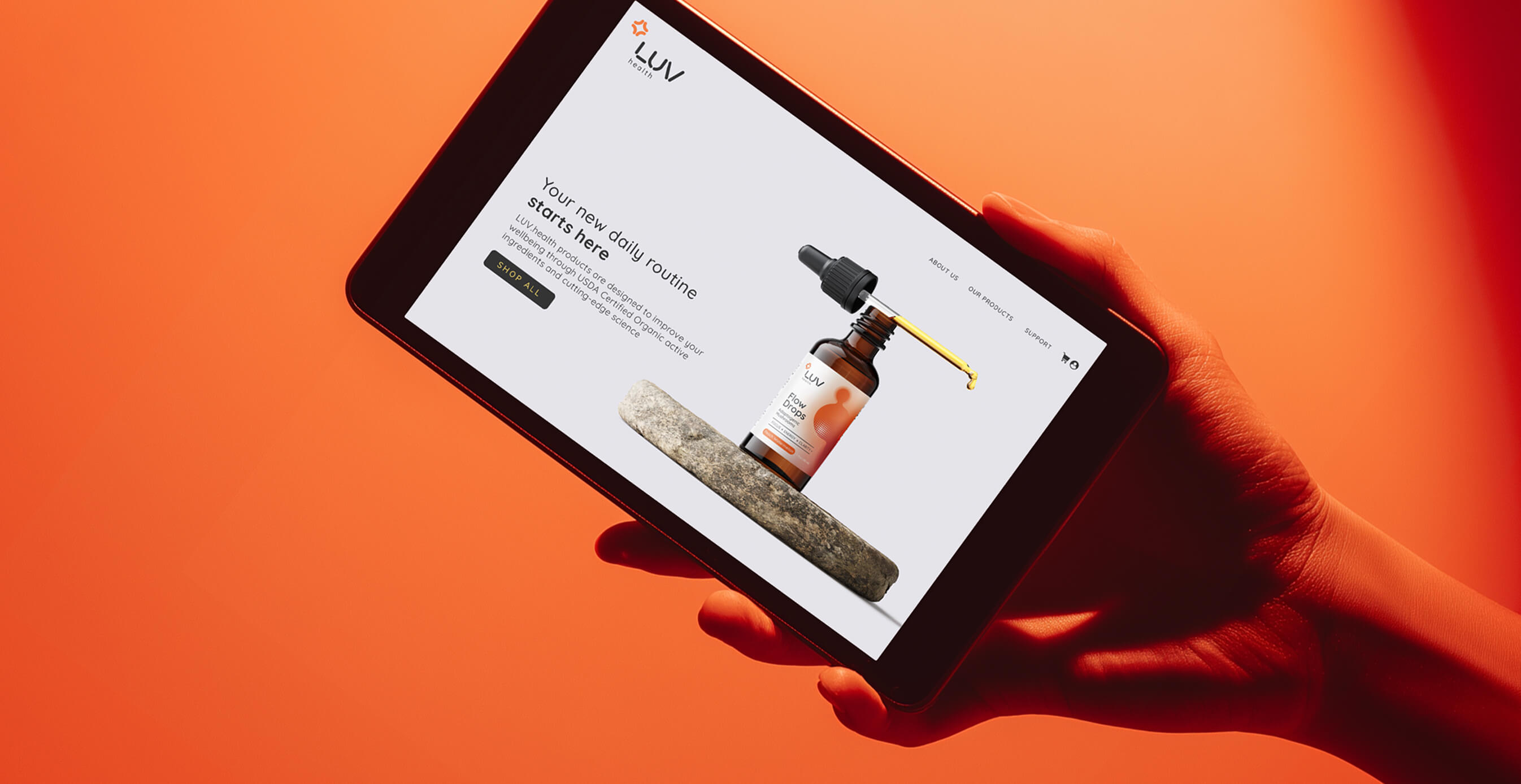 A hand holding a tablet displaying the LUV Health website featuring a wellness product dropper bottle on an orange background.