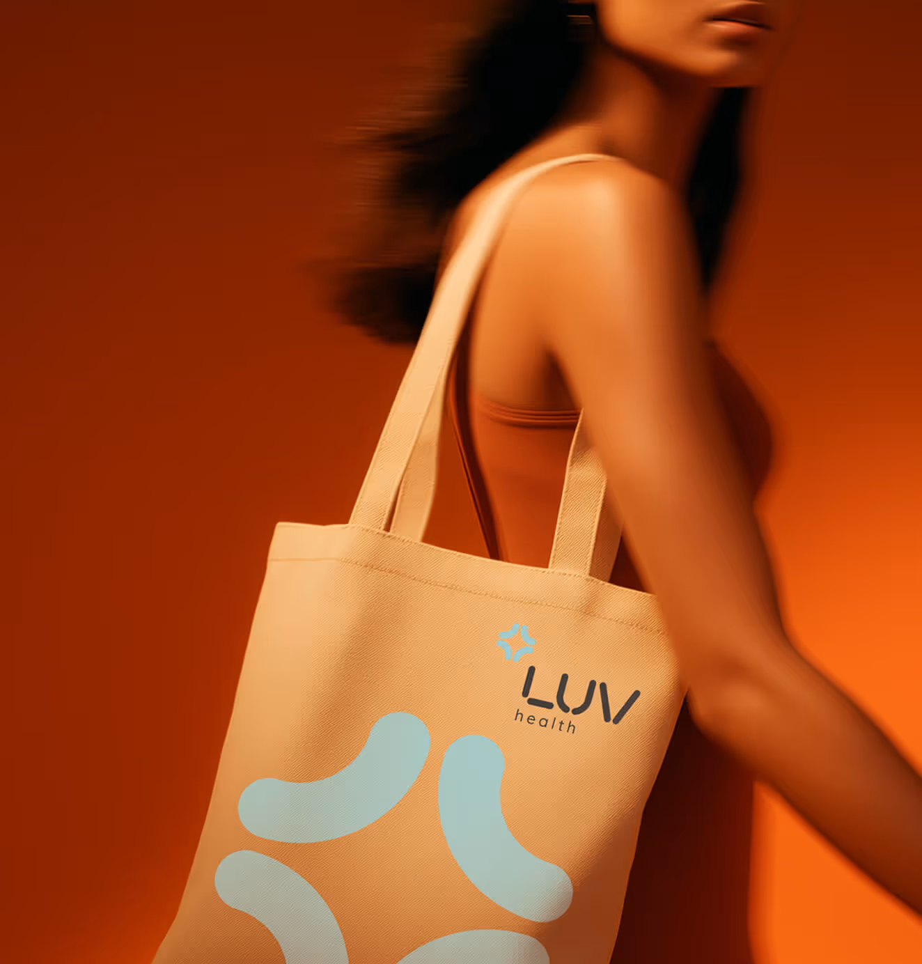 A woman wearing a tan tote bag with the LUV Health logo and abstract blue design, set against an orange background.