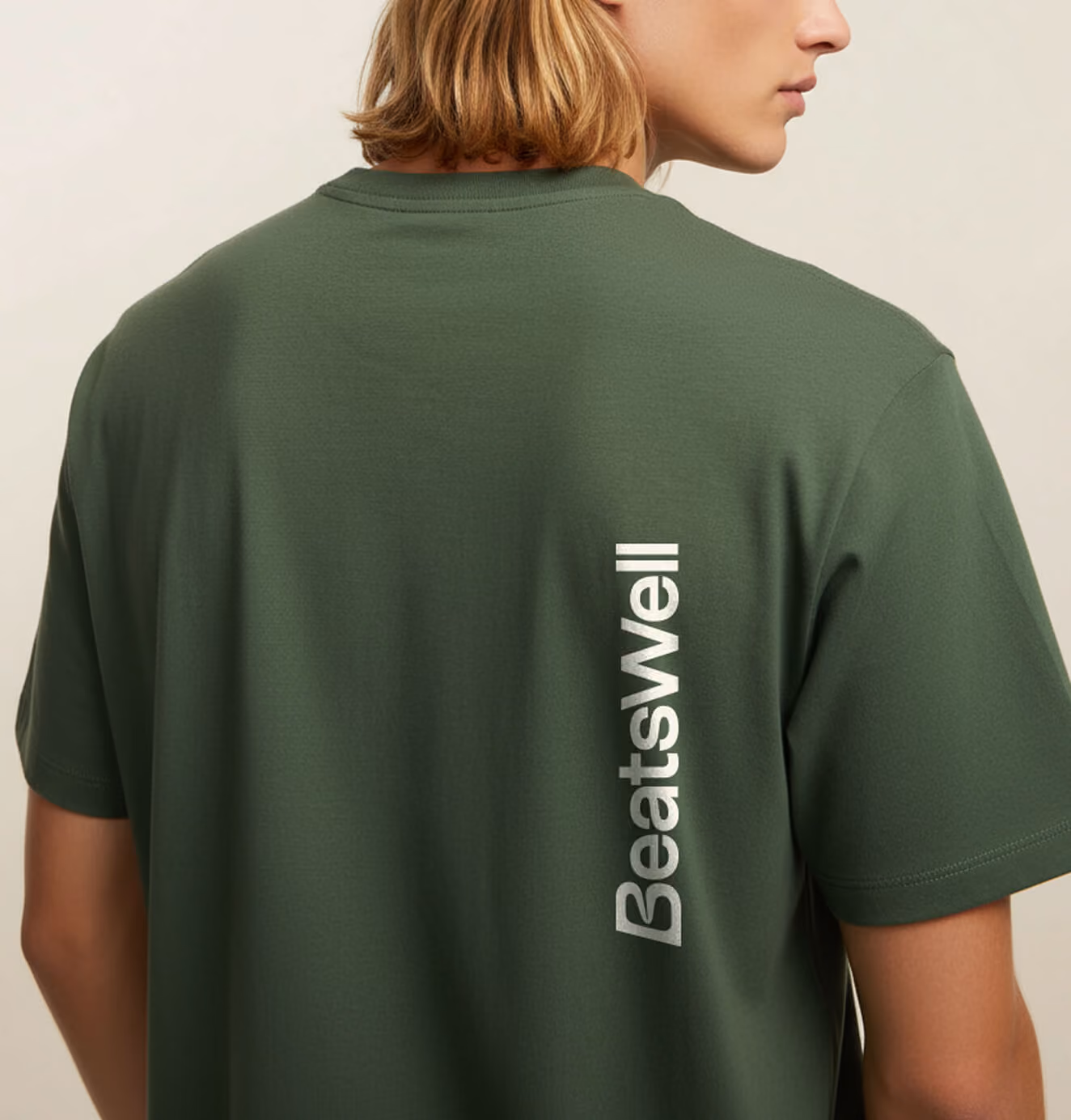 Back view of a person wearing a dark green BeatsWell t-shirt with the logo printed vertically along the spine.