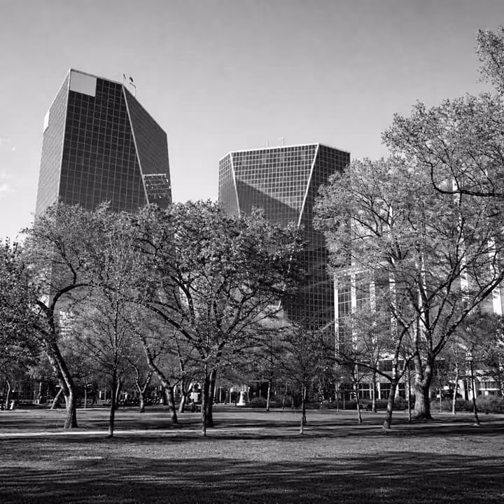Black and white photo of downtown Regina skyline with modern glass office towers rising behind a tree-filled urban park in Saskatchewan.