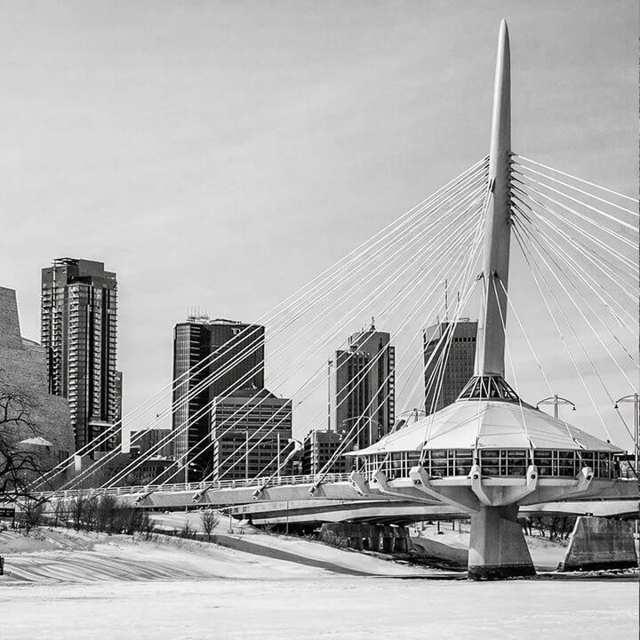 Black and white photo of Winnipeg skyline featuring the Esplanade Riel pedestrian bridge over the Red River.