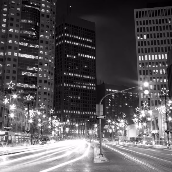 Black and white downtown Winnipeg street scene at night with illuminated office towers and light trails.