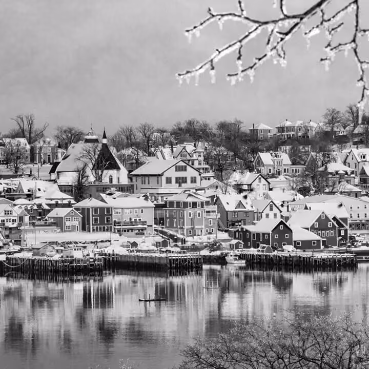 Black and white waterfront view of Lunenburg, Nova Scotia, with historic colorful homes reflected in the harbor.