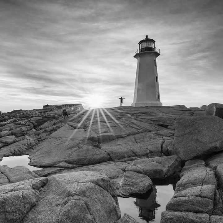 Black and white photo of Peggy’s Cove lighthouse on rugged coastal rocks in Nova Scotia at sunrise.