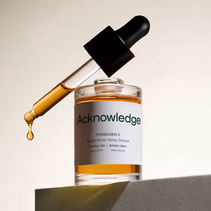 Minimalist product photography of an Acknowledge CBD oil bottle with glass dropper releasing golden hemp extract against a neutral background.